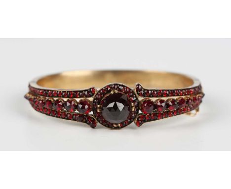 A Bohemian garnet oval hinged bangle, mounted with the principal Bohemian garnet to the centre between tapered sides, on a sn