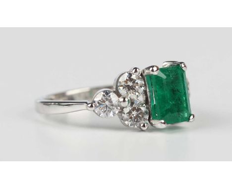 An emerald and diamond ring, claw set with the cut cornered rectangular step cut emerald between circular cut diamond three s