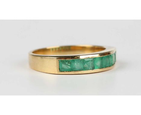 A gold and emerald ring, mounted with a row of seven square step cut emeralds, detailed ‘18K’, weight 4.6g, ring size approx 