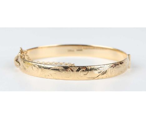 A 9ct gold oval hinged bangle with scroll engraved decoration, on a snap clasp, fitted with a safety chain, London 2003, weig