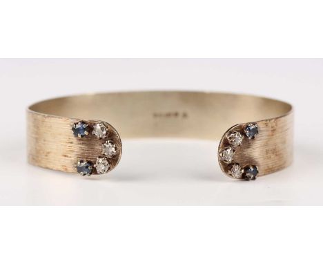 A 9ct white gold bangle, each terminal mounted with three cushion cut diamonds and two cushion cut sapphires, London 1983, we