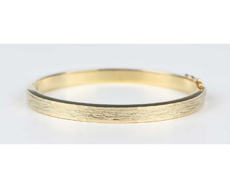 A 14ct gold oval hinged bangle with textured decoration between facet cut edges, on a snap clasp, weight 21.8g, inside width 