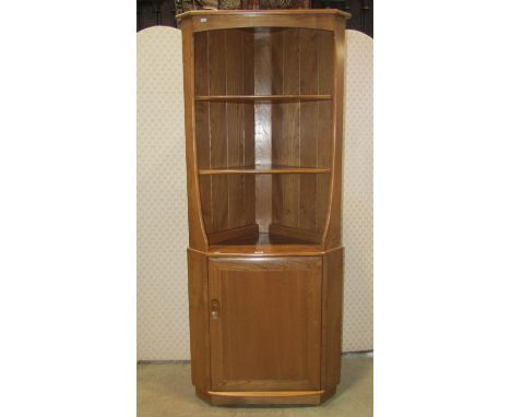 A blonde Ercol elm freestanding corner cupboard partially enclosed by a rectangular door with dished handle beneath two fixed