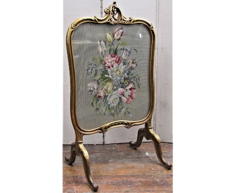 A fire screen, the carved and gilded frame in the rococo manner and raised on four scrolled supports enclosing a hand worked 