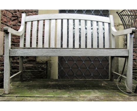 A weathered teak two seat garden bench with curved drop in slatted seat and back beneath an arched rail, 120cm long 