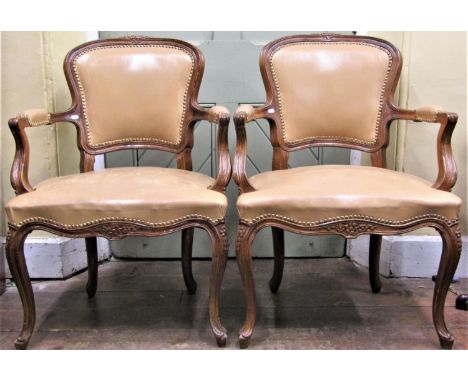 A pair of French open armchairs with carved and moulded frames, upholstered in a light tan coloured hide and raised on shaped