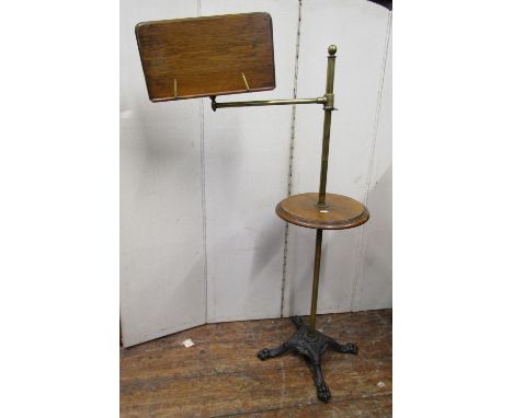 A Victorian reading stand with cast iron base, lions paw feet, the brass column supporting a circular oak panel and an adjust