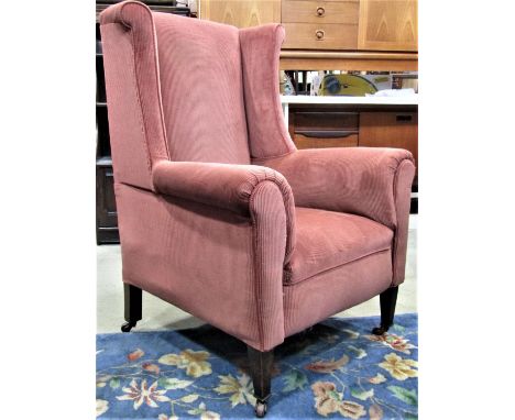 A late Victorian /Edwardian shallow winged back armchair with rolled arms, upholstered finish raised on square tapered forele