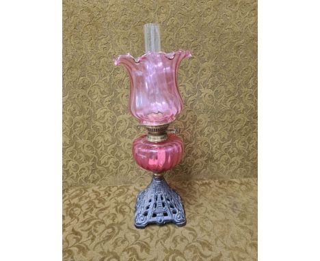 Victorian cranberry glass oil lamp with pierced cast iron base.  Wrythen form vessel and shade.