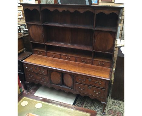 A George III oak dresser with rack, the base with four drawers and two doors between, the rack section with cupboard doors an