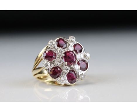 Ruby and diamond 14ct yellow and white gold set flower head ring, the central oval mixed cut ruby measuring approx 6.5mmx 5.5
