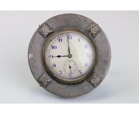 Silver dressing table clock of circular form, four raised cast square plaques, cream dial and seconds dial, blue Arabic numer