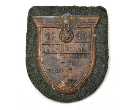 A Third Reich bronzed zinc Kuban arm shield, on field grey cloth patch with original paper backing. GC (very minor corrosion)