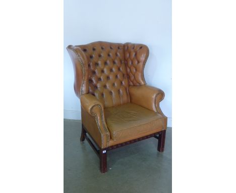 A modern tan leather covered button back armchair with mahogany legs