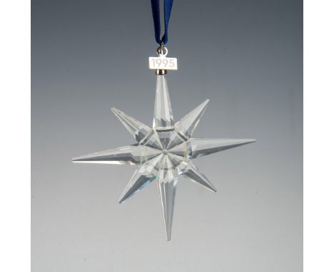 A clear, faceted eight-point snowflake ornament, hanging from a satin navy blue ribbon, with a metal tag impressed with 1995.
