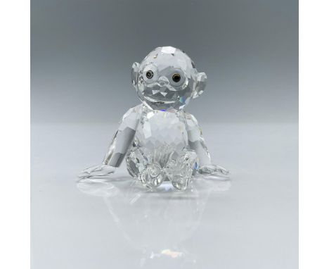 A clear crystal figure depicting a young chimpanzee that is sitting on his bottom with his arms outstretched. Swarovski backs
