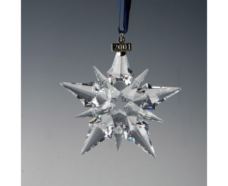 A clear, faceted ten point snowflake adornment featuring a metal tag with 2001 impressed on it, hanging from a navy blue ribb