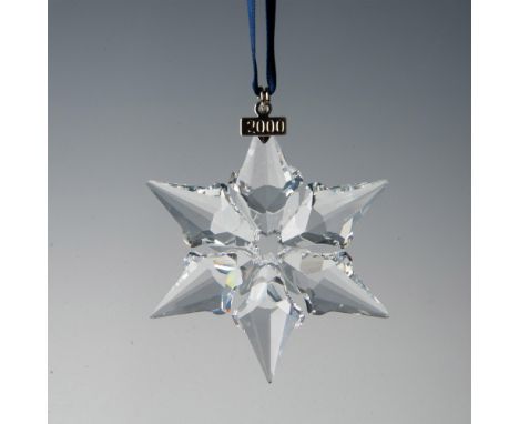A clear, faceted six point snowflake adornment featuring a metal tag with 2000 impressed on it, hanging from a navy blue ribb
