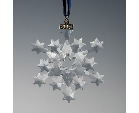 A clear, faceted star snowflake adornment featuring a metal tag with 2004 impressed on it, hanging from a blue satin ribbon. 