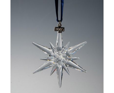 A clear, faceted twelve point snowflake adornment featuring a metal tag with 2005 impressed on it, hanging from a navy blue s