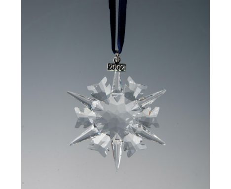 A clear, faceted six-point snowflake adornment hanging from a navy blue ribbon, featuring a metal tag with 2002 impressed on 