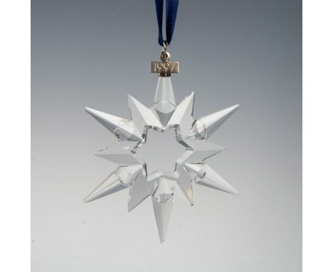 A clear, faceted twelve-point snowflake ornament, hanging from a satin navy blue ribbon, with a metal tag impressed with 1997