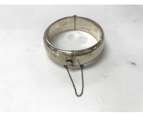 A silver bangle with safety chain and scroll pattern. Weight approx 28.4g