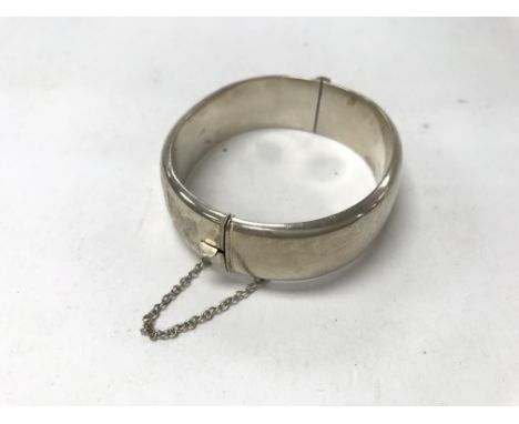 A silver bangle with leaf design and safety chain. Weight approx 31.2g