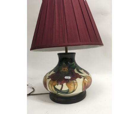 A Moorcroft table lamp decorated with flowers and foliage with red shade .