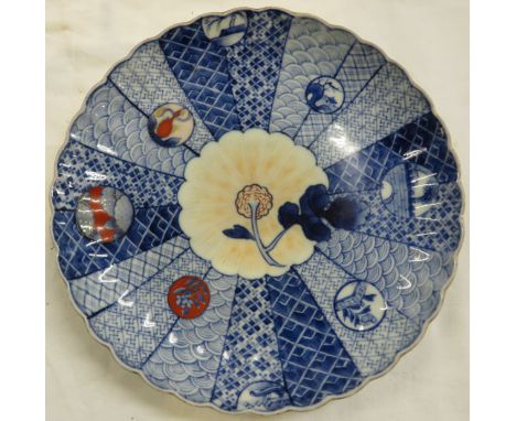 A circular porcelain plate with wavy rim, painted in blue and red with flower and divisions of scales and hatching, circular 