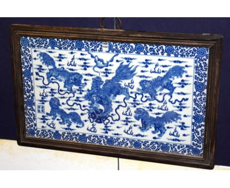 A Chinese blue and white ceramic panel, depicting dragons in foliage, with character marks on white ground, in wooden frame, 