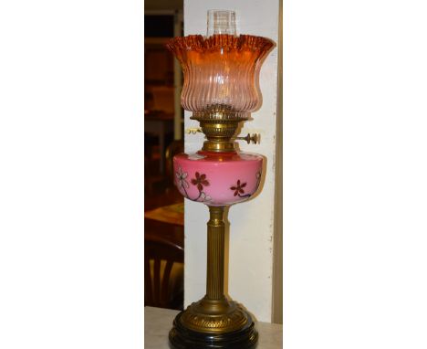 A Victorian oil lamp, with amber tinted frilly glass shade, above a handpainted floral pink opaque glass reservoir, raised on