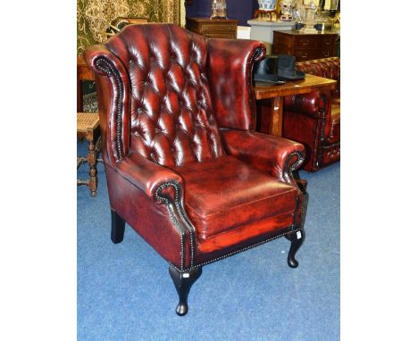 A Chesterfield ox blood wing back armchair, with button back, cushion arms, raised on cabriole supports, 111cm high x 86cm wi