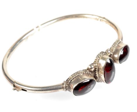 A silver bangle set with three garnets.