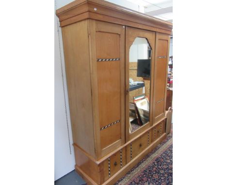 A late Victorian light wood triple wardrobe with central mirrored door and painted decoration to simulate inlay.