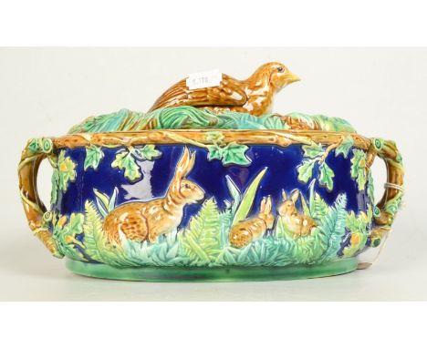 A Majolica game pie dish by George Jones, the lid with a quail finial on a ground of ferns, the base with rabbits and twin na