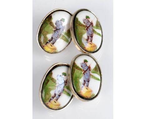 A pair of fisherman cuff-links each silver and set with a ceramic oval showing an angler on a river bank at his feet a creel.