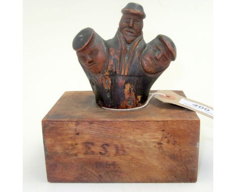 A country craft carving possibly a walking stick finial, it shows three hatted figures, it is now mounted on a yew wood block