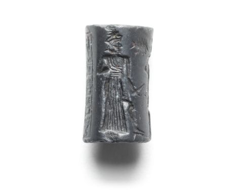  An Old Babylonian haematite cylinder seal Circa 1800-1600 B.C.Engraved with three figures comprising a worshipper wearing a 