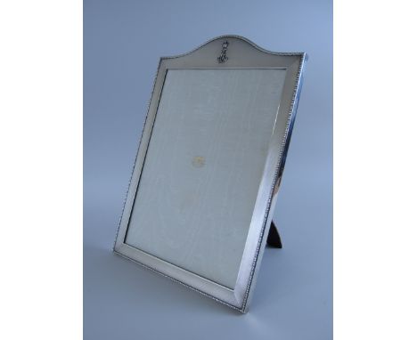 A George V silver Photograph Frame with engine turning inside leaf and berry border bearing embossed monogram to arched top, 