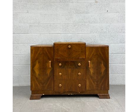A mid 20th century Art Deco style walnut drinks cabinet having a stepped top over a central quarter veneered fall front mirro