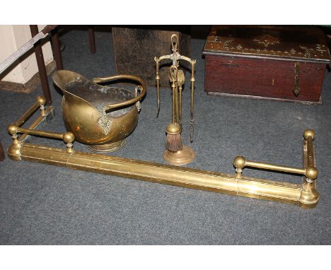 A brass fire fender, 123cm, a set of four fire tools on stand, and a brass helmet shape coal scuttle with swing handle