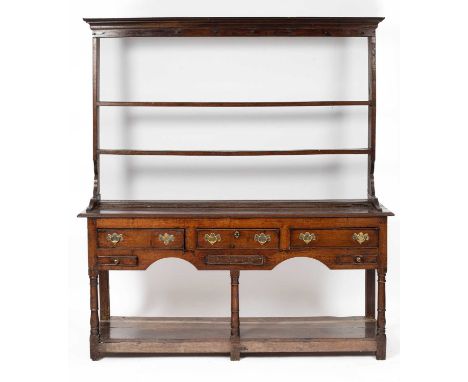 A Georgian oak dresser having a set of shelves over a base with a moulded top over three cock-beaded frieze drawers with bras