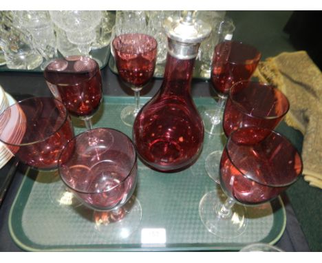 A cranberry glass decanter and stopper, along with seven cranberry glass wine glasses with clear stems