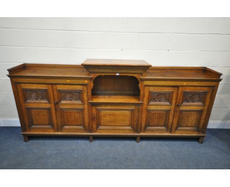 A LONG EARLY 20TH CENTURY OAK BOOKCASE, the double fielded and carved panel doors, below a gallery, both flanking an open sec