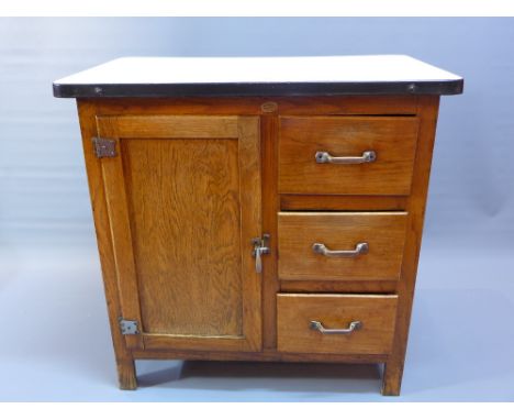 An early 20th Century oak kitchen side table with white enamel top above cupboard door and three drawers raised on square leg