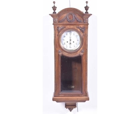 An early 20th Century walnut cased wall clockWith an arched pediment above a 7" enamel dial painted with Arabic numerals, hav