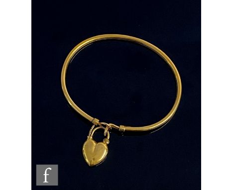 An early 20th Century 9ct stiff bangle terminating in heart shaped padlock, with a 9ct heart shaped almandine garnet and seed