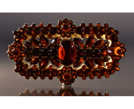 A garnet and gold plated silver brooch, multi layered arching floral body pave encrusted with cut and cabochon vibrant red ga