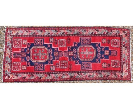 A Persian red ground carpet with central geometric medallions and repeating borders, 337 x 142 cm